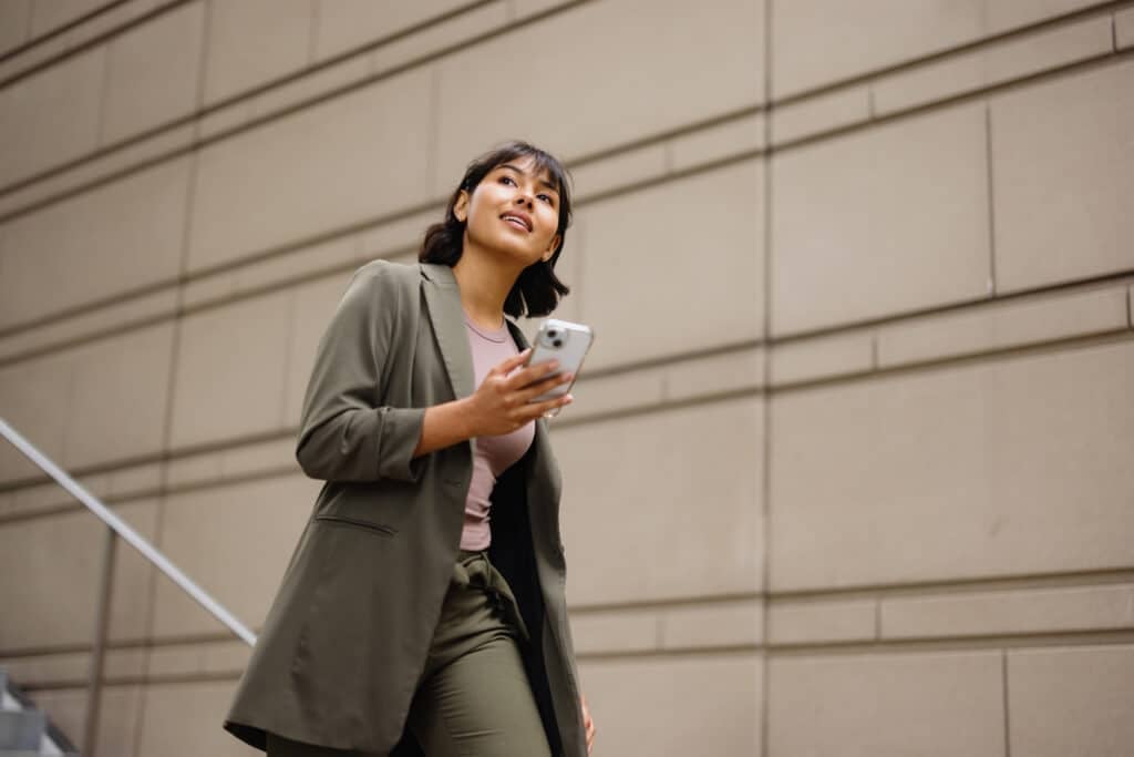 Young businesswoman confidently walking down the stairs of a modern office building, engaging with her smartphone while commuting to work