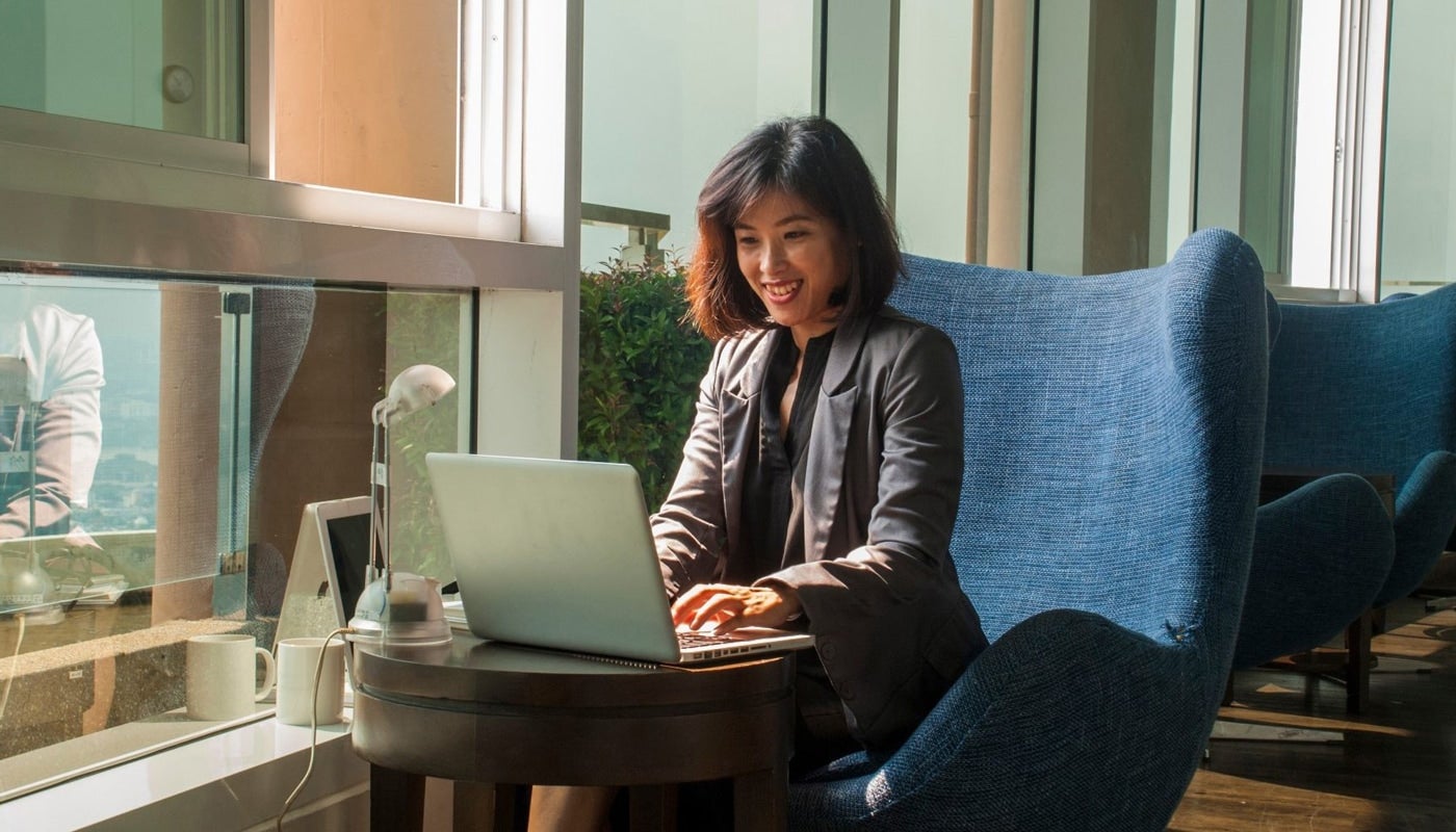 Businesswoman smiling while working with a laptop and a lamp placed beside her in the office