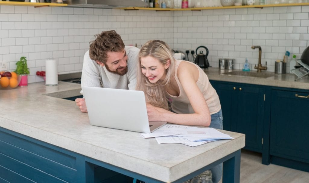 Young couple at home using a laptop computer and looking very happy looking at credit history together and discussing credit score