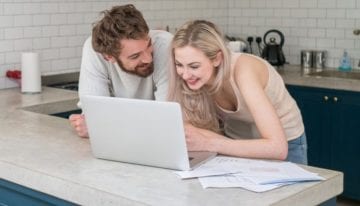 Young couple at home using a laptop computer and looking very happy looking at credit history together and discussing credit score
