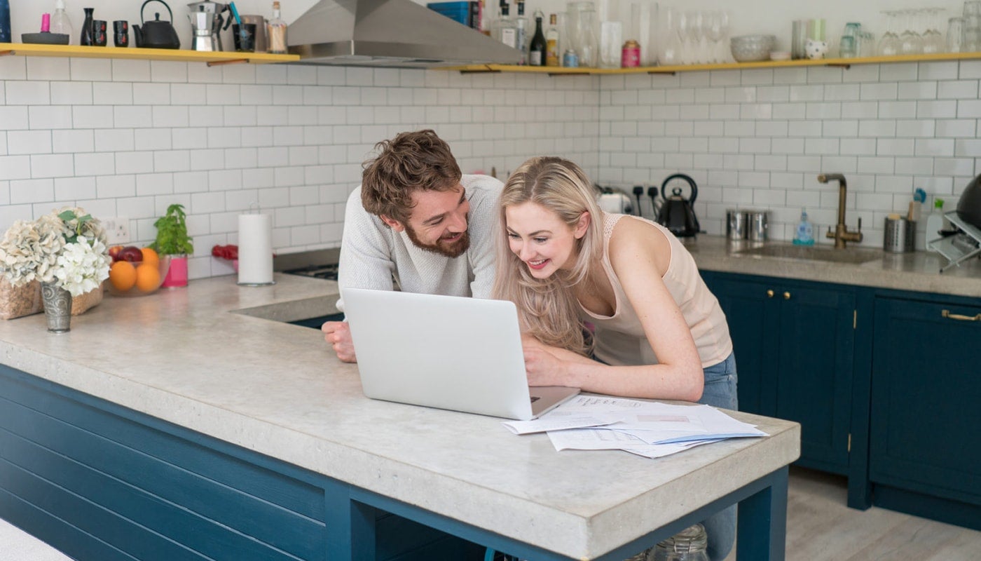Young couple at home using a laptop computer and looking very happy looking at credit history together and discussing credit score
