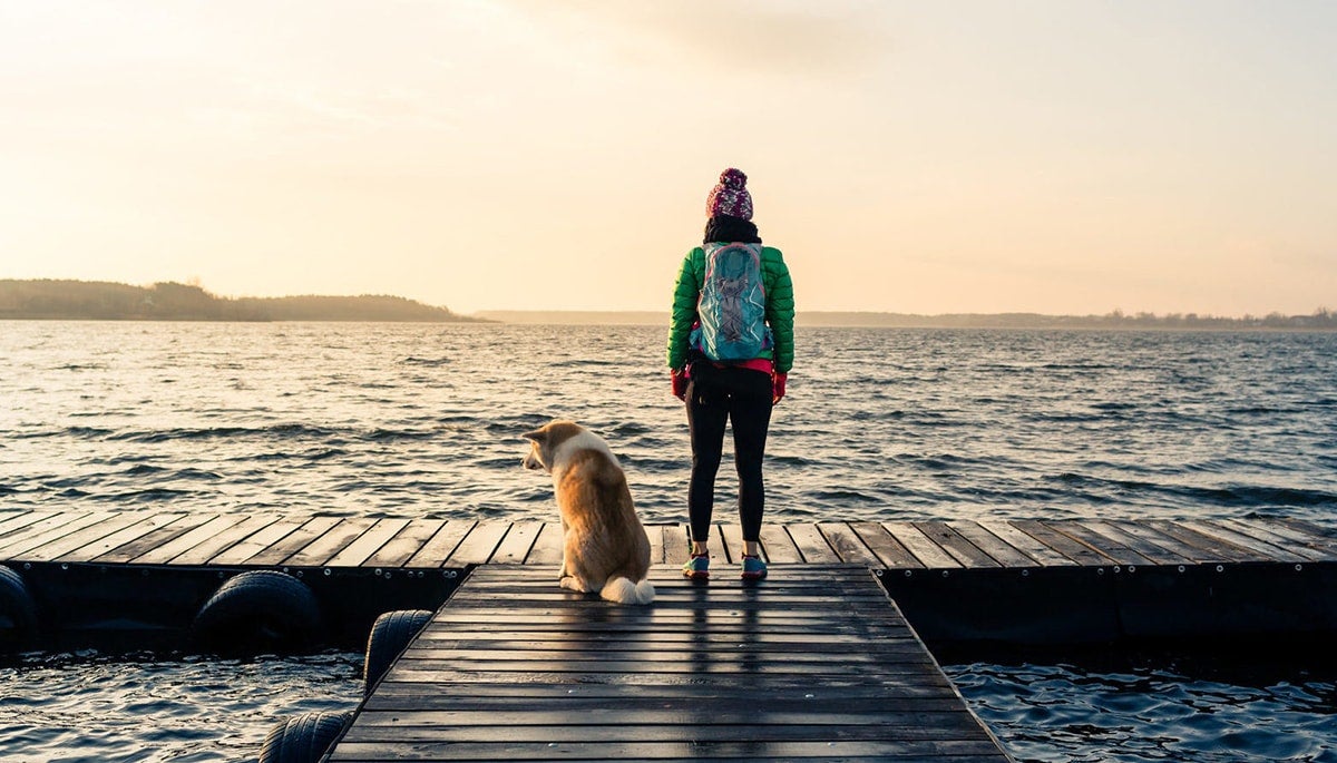 Woman with dog enjoying sunrise and lake. Relaxing and thinking about college major.