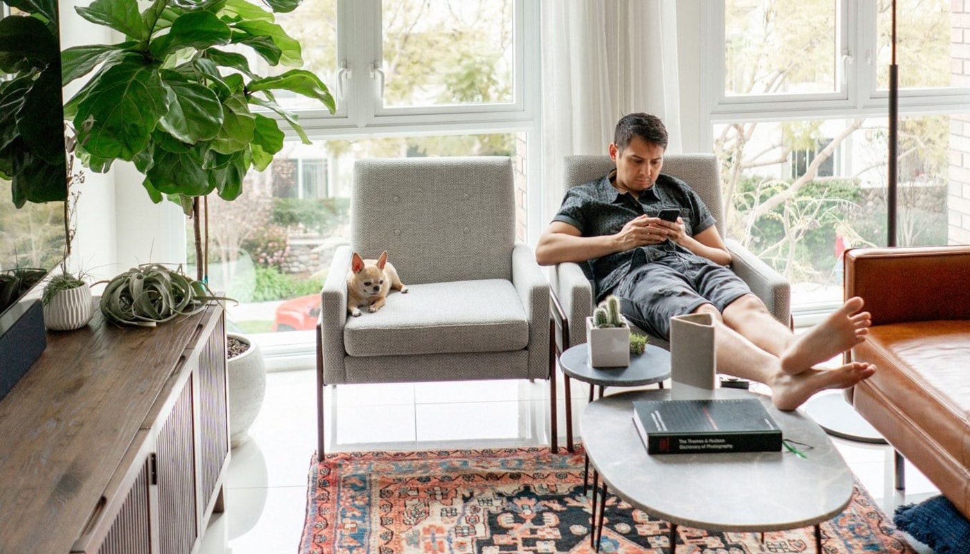 Young guy using his mobile phone in his loft with his dog sitting next to him