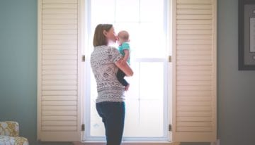 Mother with child looking at window and kissing baby