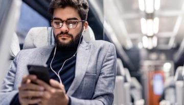 Young man reading an article on his phone and listening to podcasts while traveling by train.