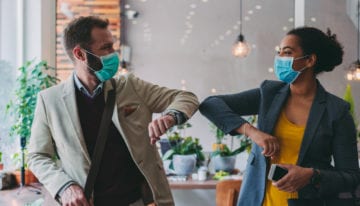 Colleagues touching elbows as they return to the office following the COVID-19 pandemic.