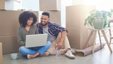 young couple using a laptop in living room with boxes