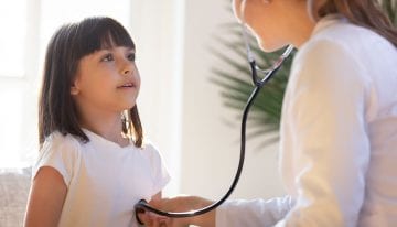 Female pediatrician listening to young girl with stethoscope