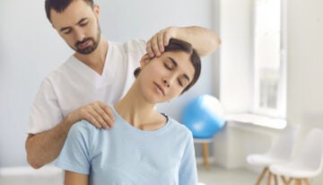 Physical Therapist, with student loans, doing neck adjustment to female patient in medical office.
