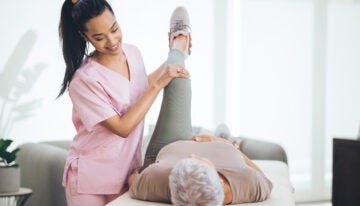 Physical therapist, who qualified for physical therapy student loan forgiveness, performs light exercises on elderly patient.