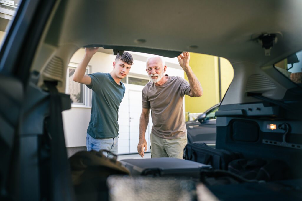 Two men Teenager and senior man grandfather grandson pack baggage luggage in trunk of the car prepare for road-trip vacation or student go to campus