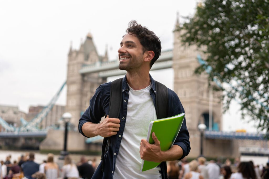 Portrait of a happy student in London holding a notebook and smiling near Tower Bridge.