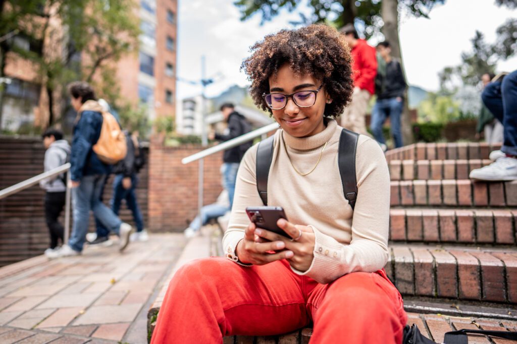 Young university student using mobile phone on stairs outdoors