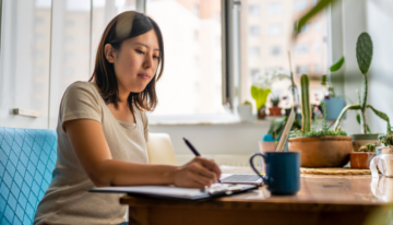 Young Asian woman sitting at a table creating a budget.