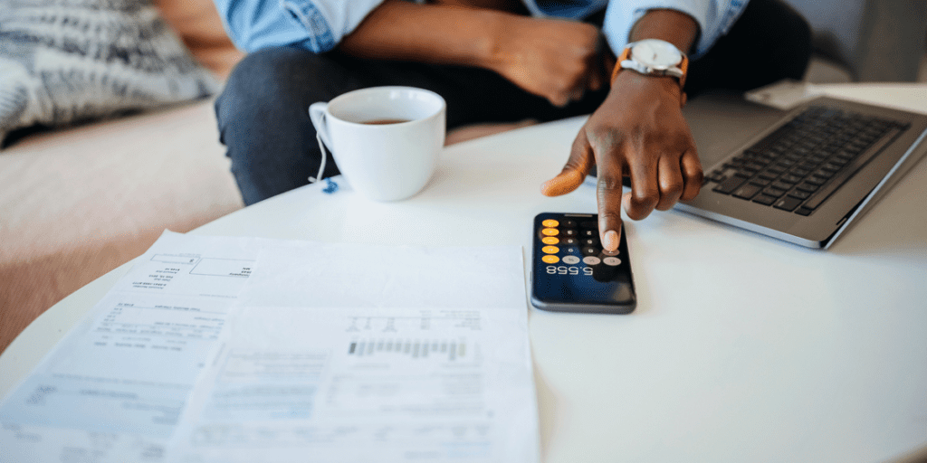 Black man using his phone calculator and looking at paperwork.