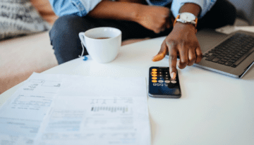 Black man using his phone calculator and looking at paperwork.