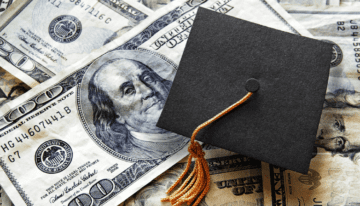 Grad cap sitting on top of piles of money.