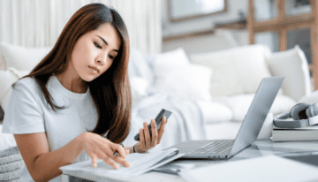 Young Asian woman sitting by couch on computer.