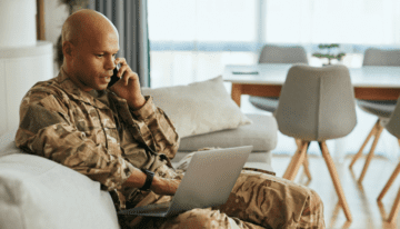 Young black male military veteran sitting on the phone with laptop.