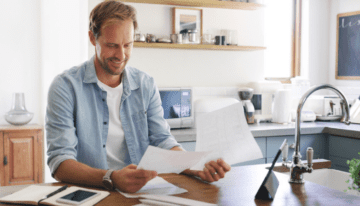 Young adult man looking at student loans and tax paperwork in kitchen.