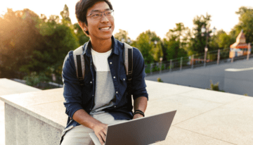 Young Asian college student sitting with laptop on college campus.