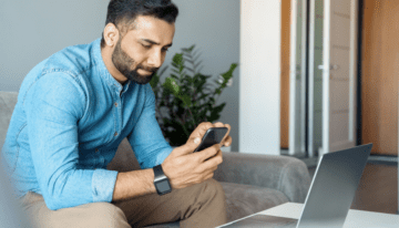 Man sitting on laptop with phone looking at student loan refinancing.