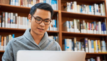 Asian male college student researching on his laptop.