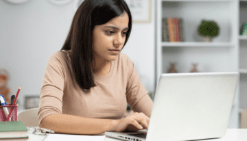 Young woman sitting at desk looking at student loan forgiveness.