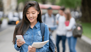 Young female Asian student looking at phone on campus.