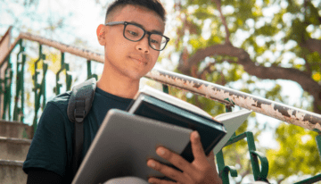 Young male college student sitting on campus reading a financial book.