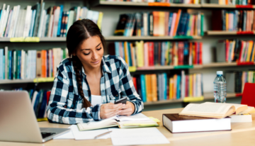 Female college student in the library looking at her phone.