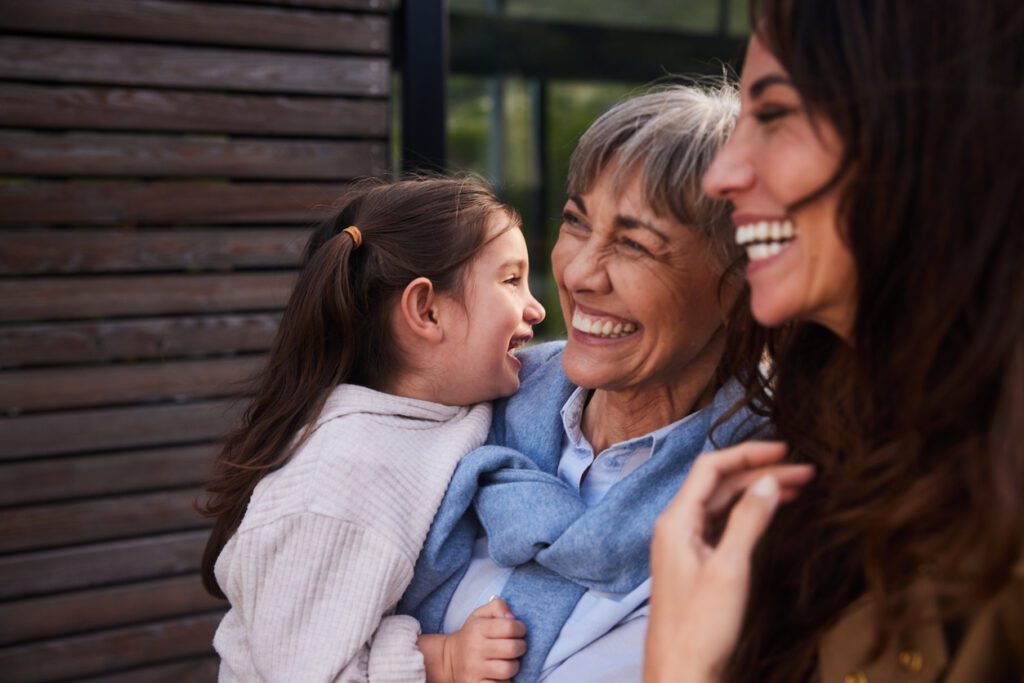 Adorable little girl laughing with her mother and grandmother outside in their back yard at home
