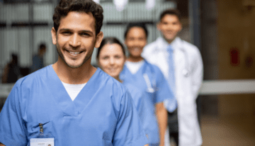 Male medical resident standing in front of other medical residents at the hospital.