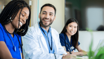 Medical residents sitting around a table talking and smiling.