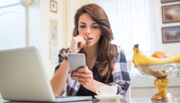 Young female adult concerned looking at phone in kitchen.