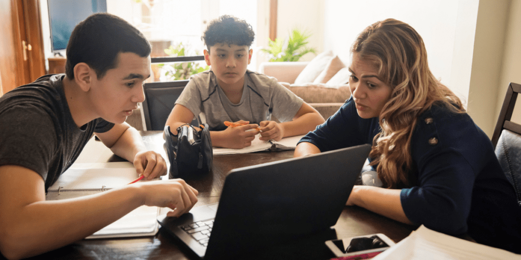 Mother homeschooling her two teenage sons at the kitchen table.