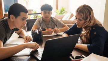 Mother homeschooling her two teenage sons at the kitchen table.