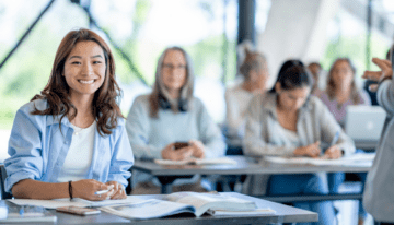 Female Asian college student sitting in classroom with other students.