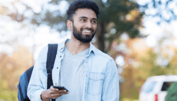 Young college male walking around college campus holding phone.