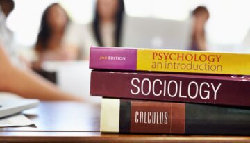 Three textbooks sitting with students who are curious how to pay for college books.