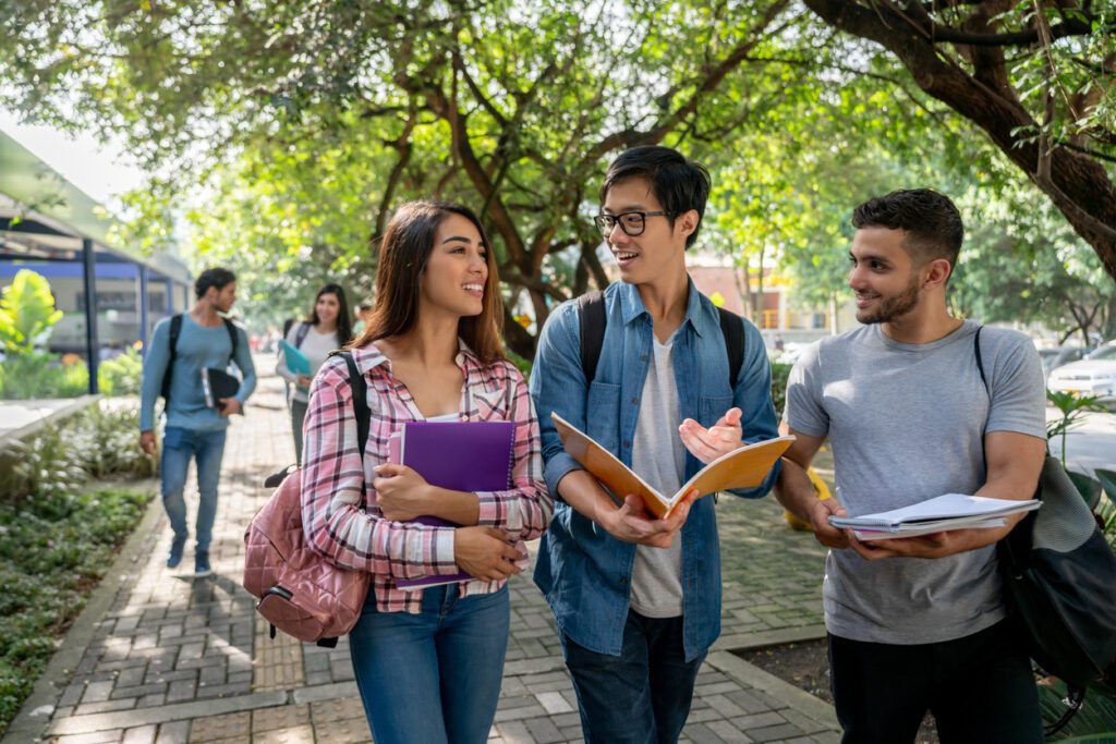 Young students at the college campus walking to class holding their books open discussing something