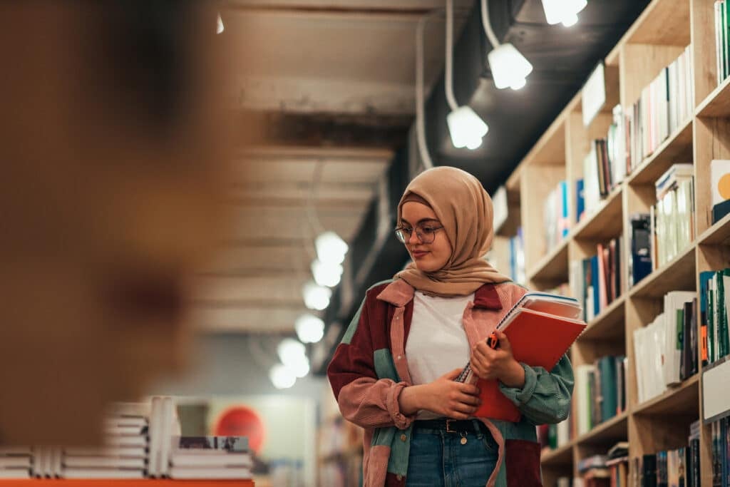 Muslim female college student looking for exam literature in library