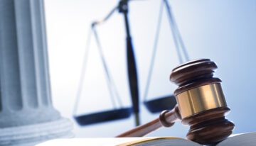 Gavel resting on book with scales in the background.