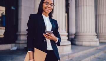 Young black female lawyer standing outside court with cell phone.