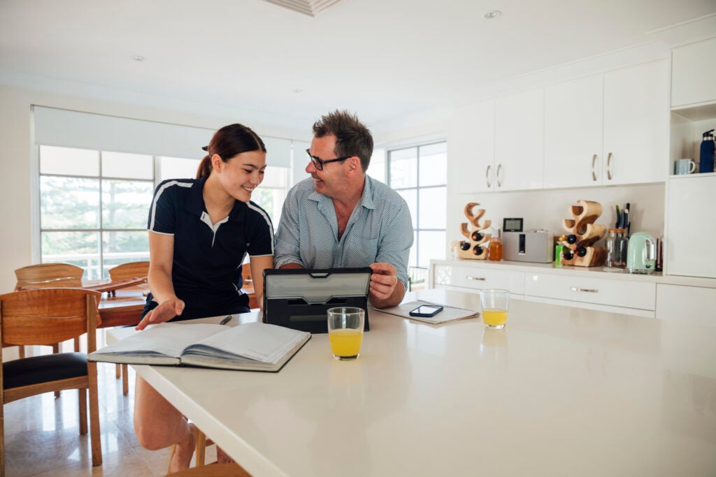 Mature caucasian father and his mixed-race daughter looking at a digital tablet and studying together in the kitchen during lockdown.