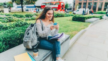 Young girl sitting on bench and using smartphone to see how soon she can refinance her student loans.
