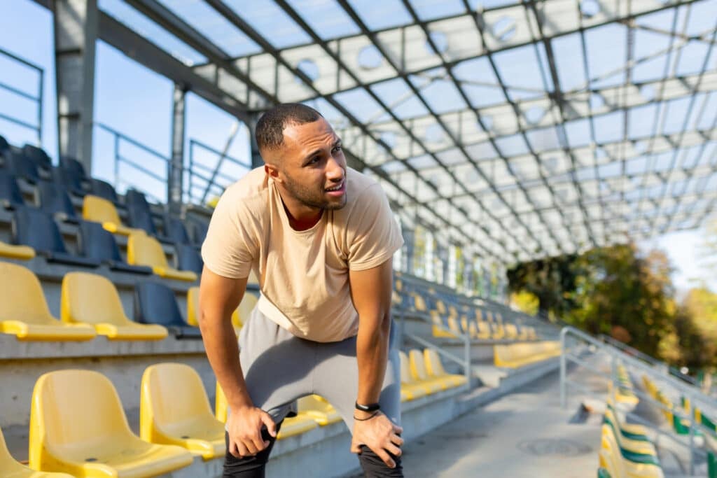 Tired hispanic athlete bent over and breathing after jogging, man doing sports on sunny day with active exercises and fitness, athlete resting after jogging.