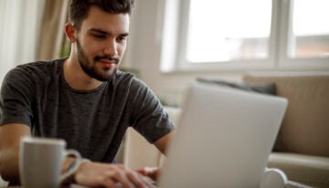 male college student changing student loan repayment plan on laptop.