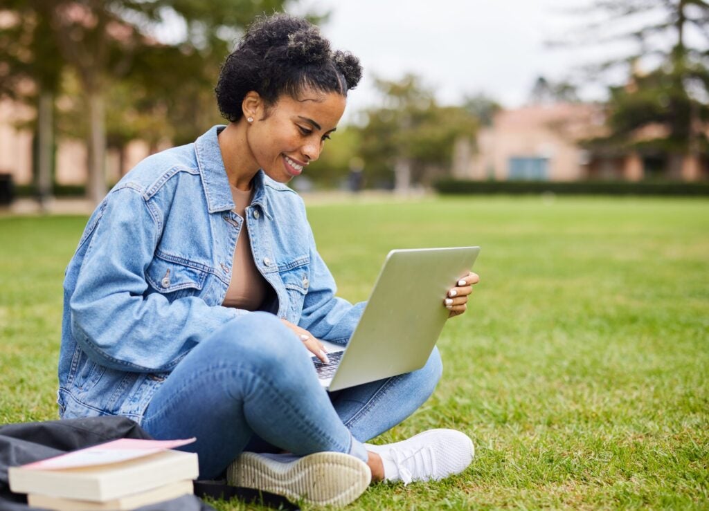 College female looking up tuition insurance on laptop outside of college