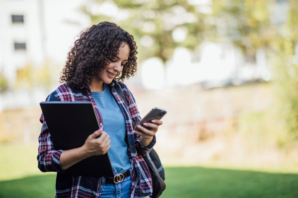 Female student looking at phone researching enrollment deposits.